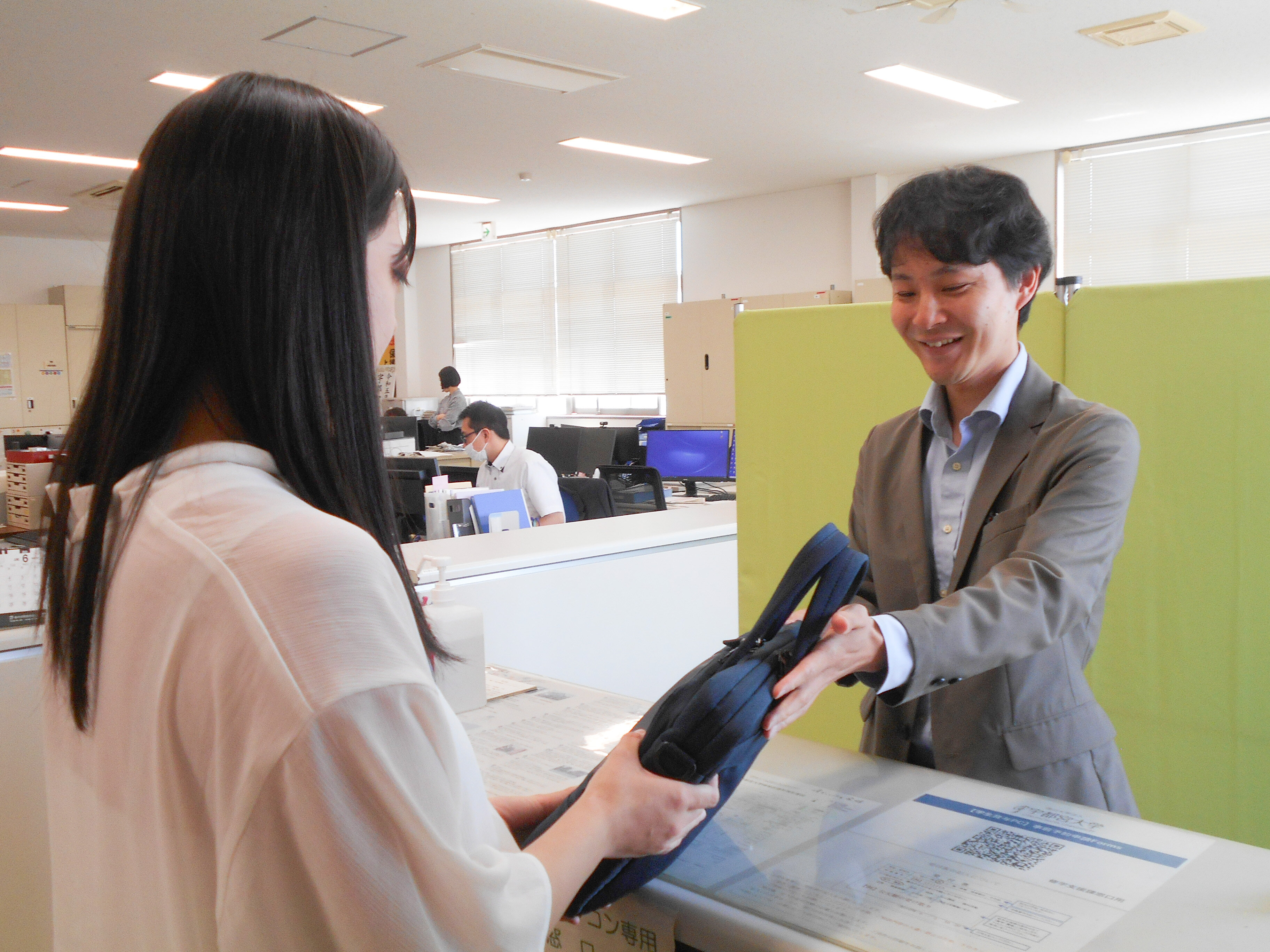 職員が窓口で学生にパソコンを貸し出ししている写真